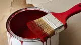 Open tin of red paint with a brush resting on top. 