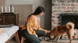Woman with a dog drinking from a bowl near a fireplace. 